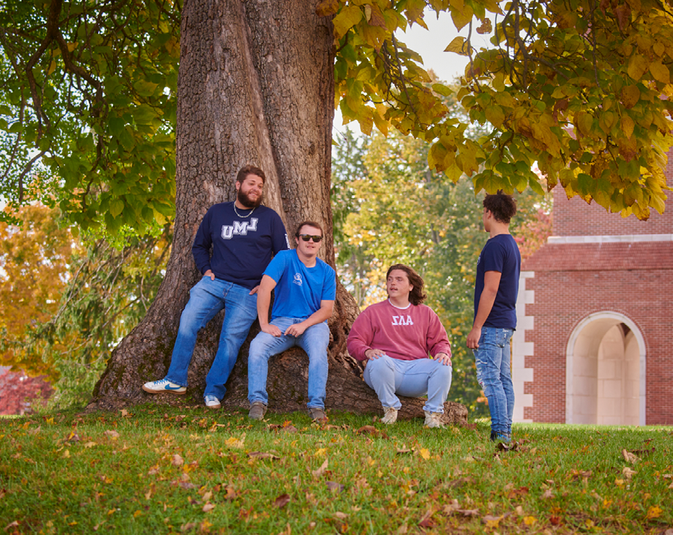 一张四名学生坐在校园一棵树旁的照片.
